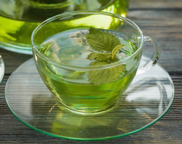 Citromfű levél tea bögrében megszórva zöld citromfű levéllel.
